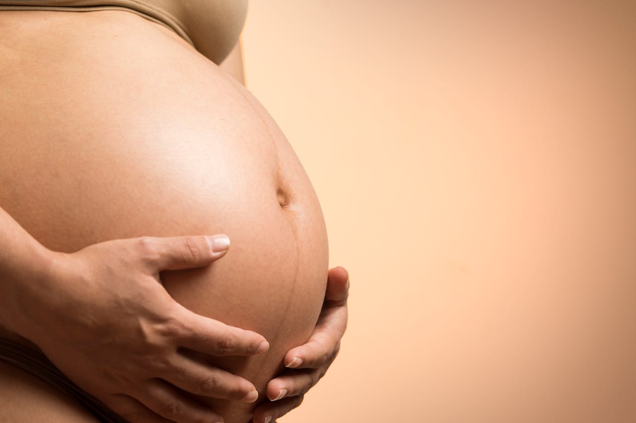 A tender close-up of a pregnant womans hands holding her belly, symbolizing maternity and love.